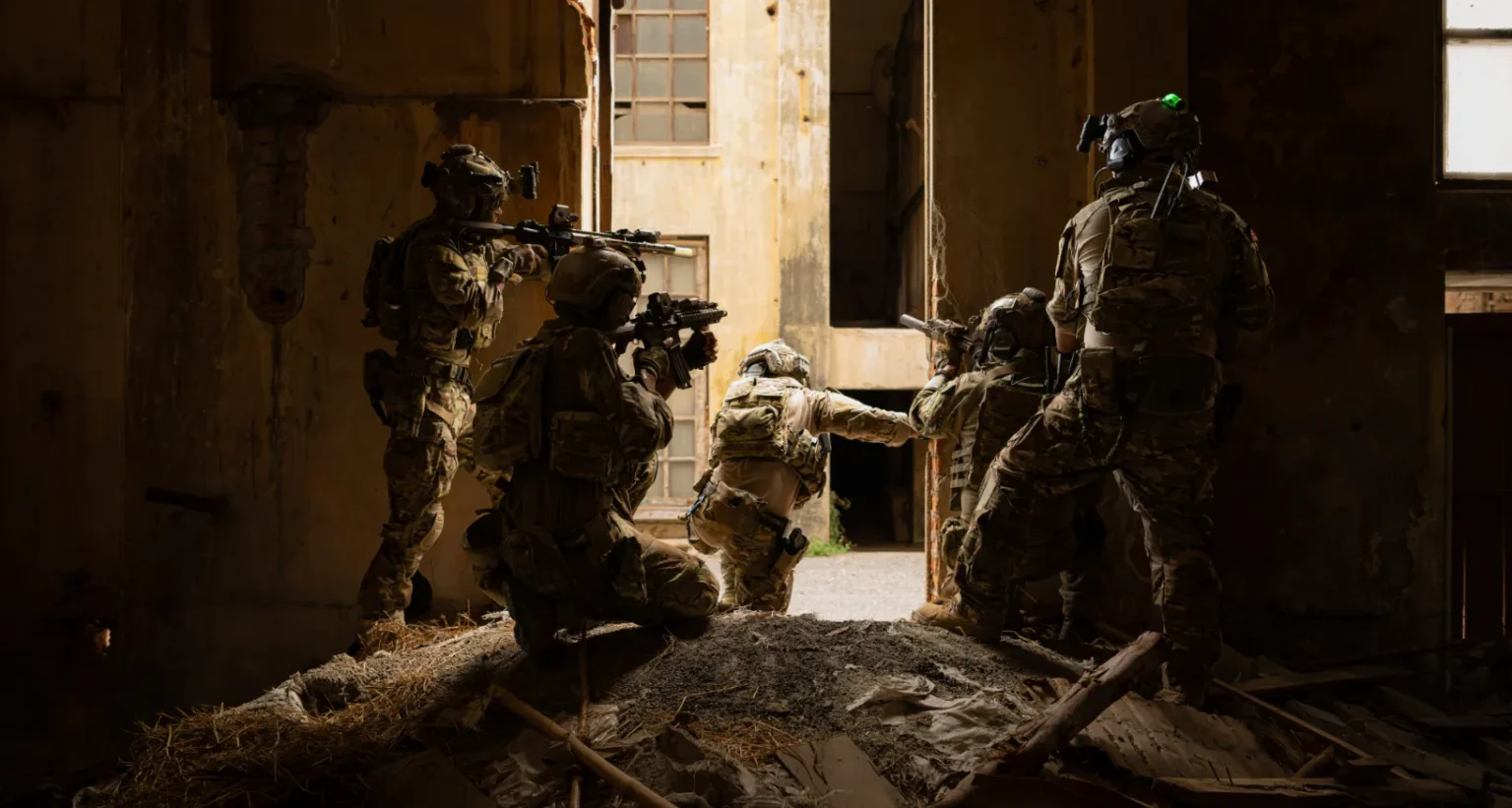 Special forces personnel in full tactical gear conducting a building clearance operation in a damaged structure under low-light conditions, representing intelligence services deployed in support of government and defense operations. Signals Intelligence and decision ready intelligence solutions empowering government and defense agencies to execute precise operations with real-time situational awareness and intelligence superiority.